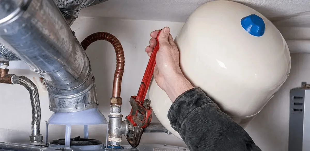 Water heater repair technician tightening plumbing connections near a tank unit in San Diego, CA